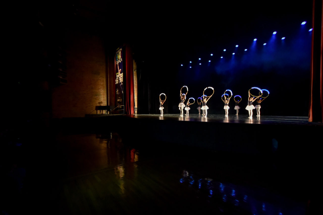 Bailarinas apresentando-se sobre palco do Teatro Polytheama, com plateia escura e iluminação somente sobre as artistas