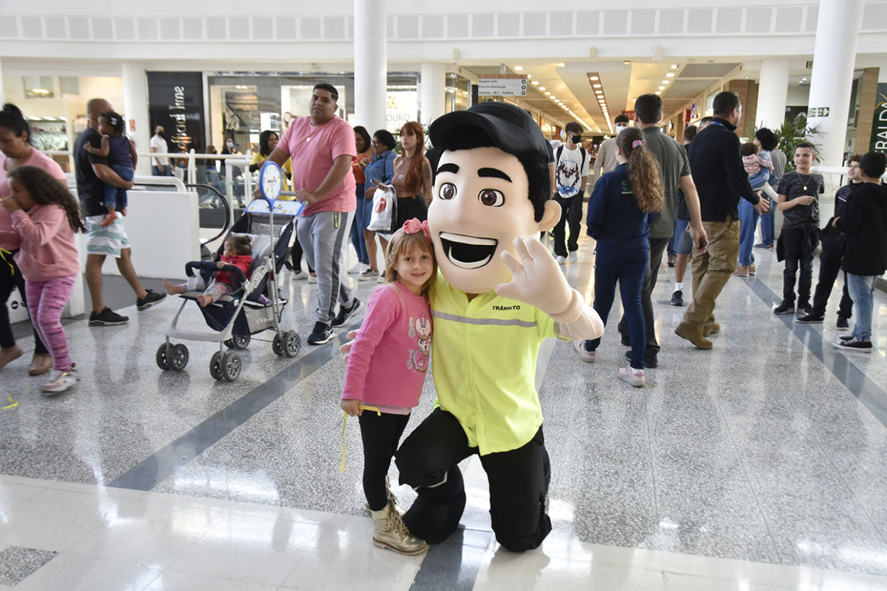 Mascote Vaguinho vestido de agente de trânsito pousa para foto ao lado de uma menina de blusa rosa no MAxi Shopping