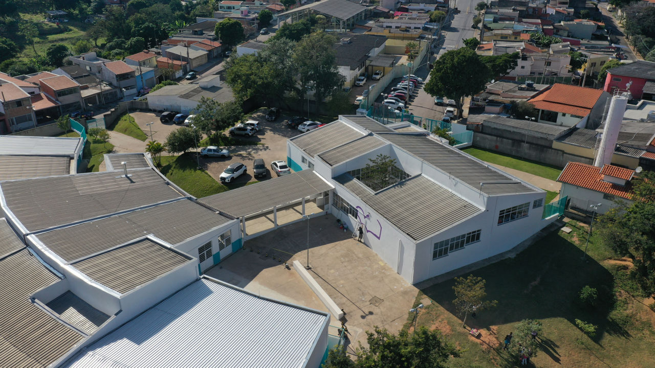 DESCRIÇÃO DA IMAGEM:
Foto aérea mostra uma grande construção com paredes brancas, área verde no entorno. É uma escola. 