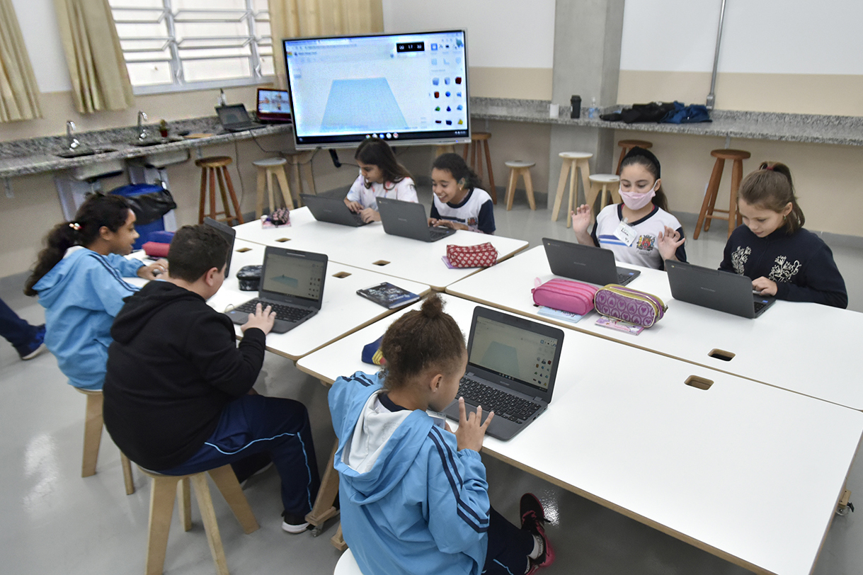 DESCRIÇÃO DA IMAGEM
Em um laboratório de escola, estudantes estão sentados em frente a mesas com computadores. Ao fundo há uma grande tela.
