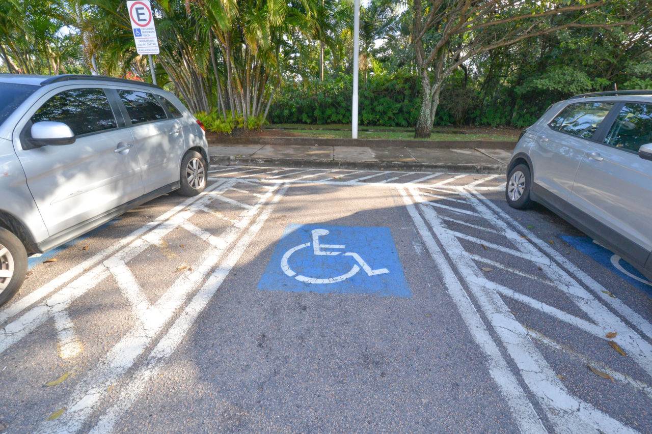 DESCRIÇÃO DE IMAGEM: foto de vaga de estacionamento de pessoa com deficiência, entre dois carros cinzas estacionados.