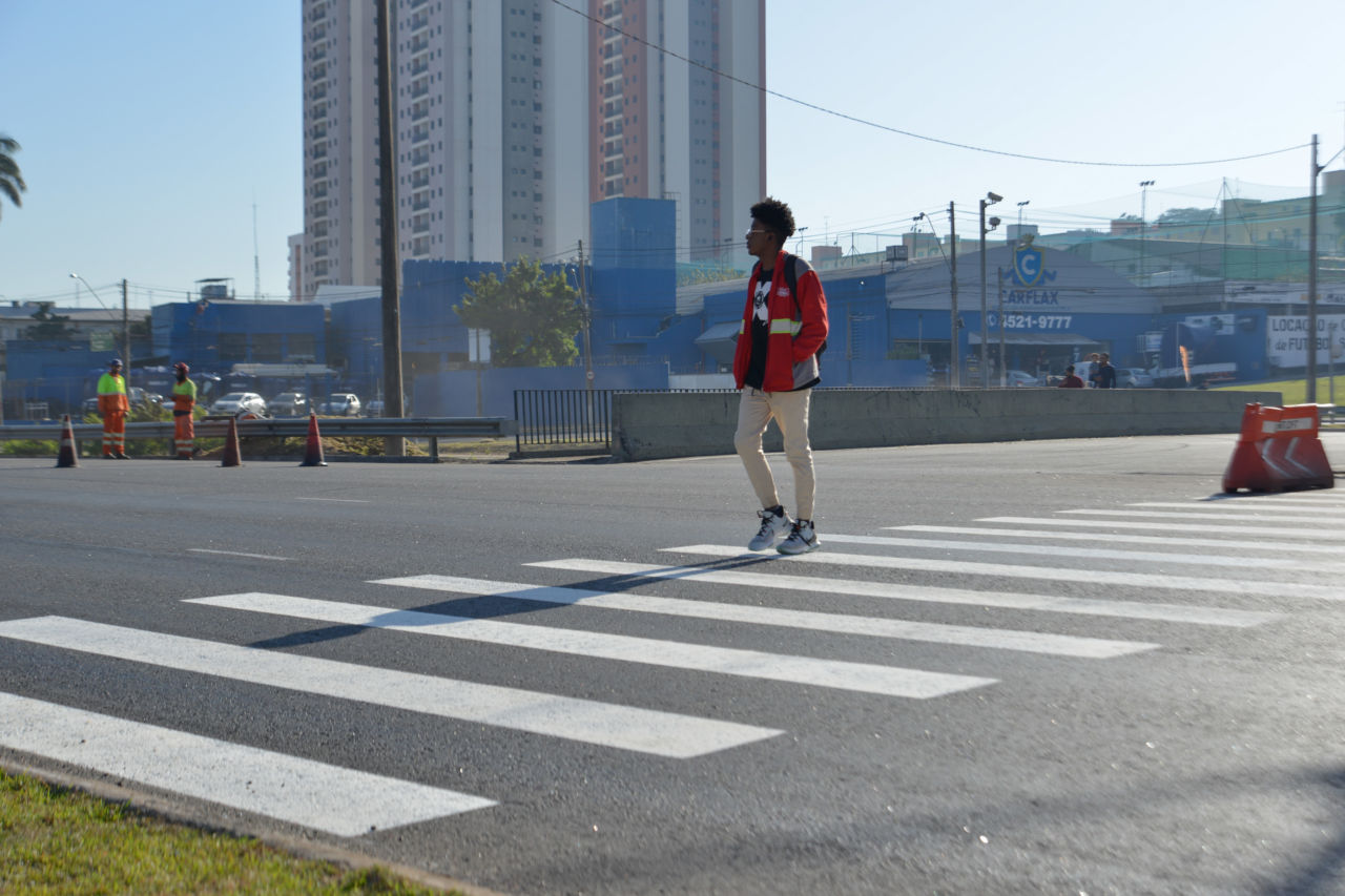 Pedestre atravessando a rua na faixa de pedestres vestido de calça bege e blusa vermelha
