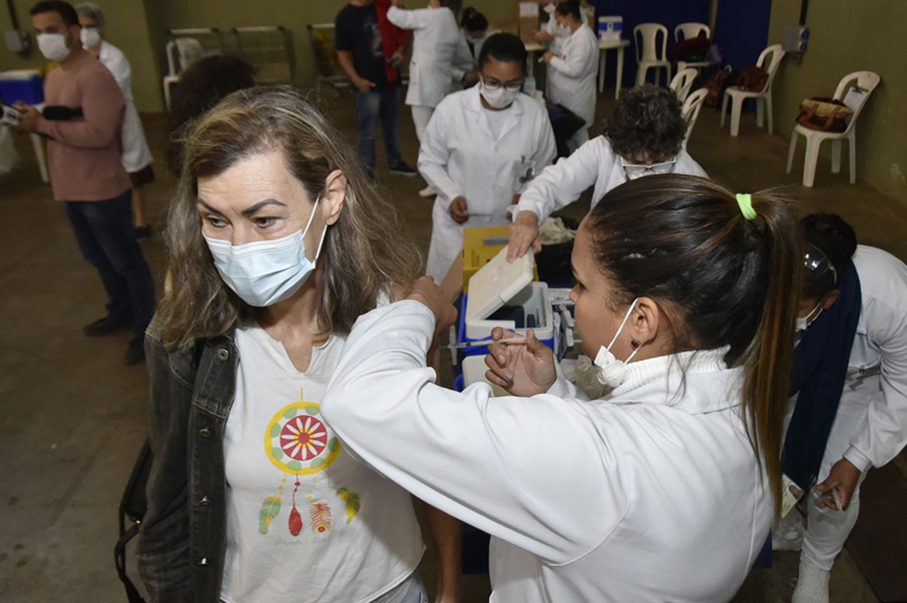 Marialba está de máscara recebendo vacina da enfermeira 