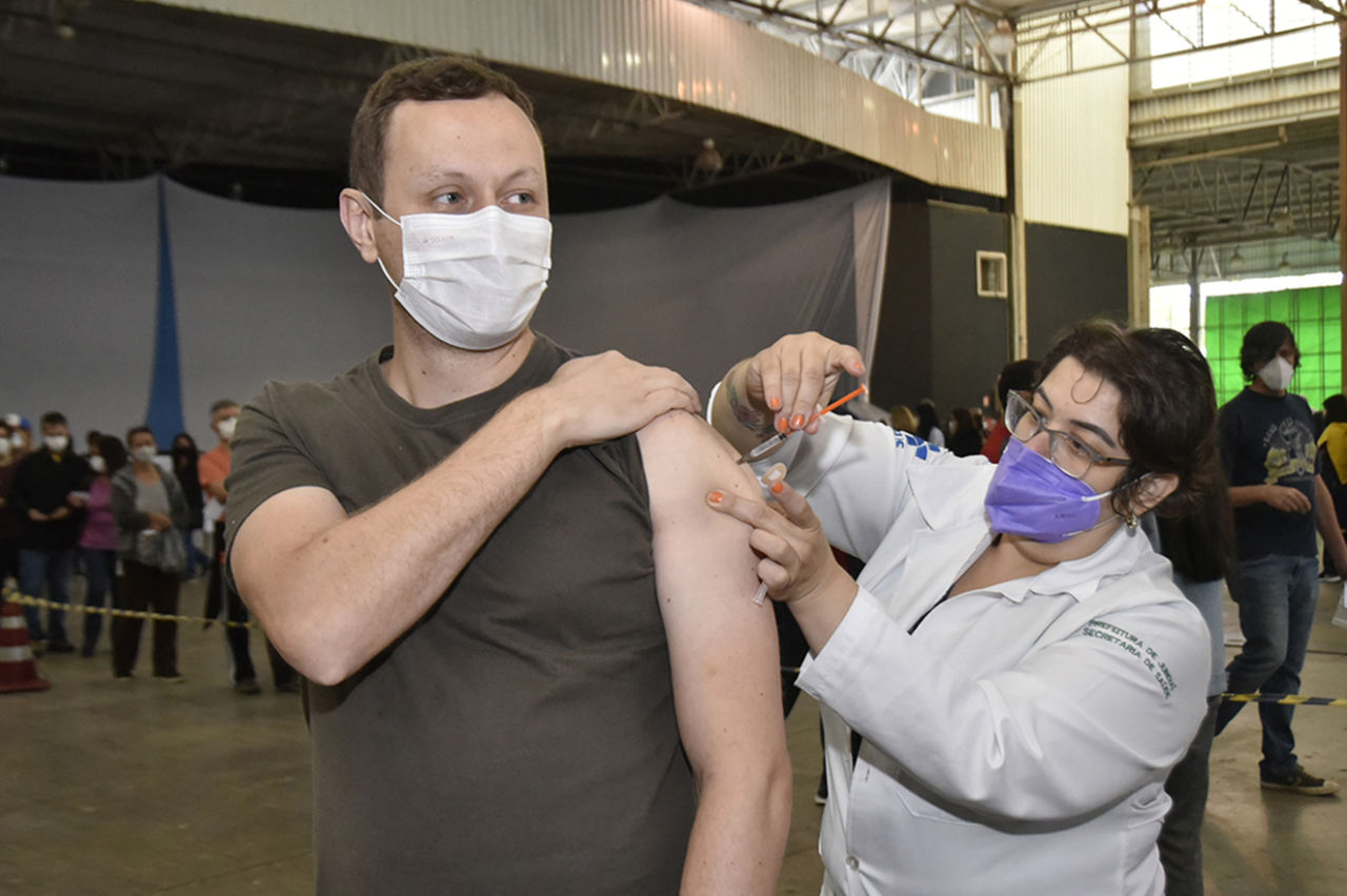 homem recebe a vacina no braço, aplicação feita por uma enfermeira 