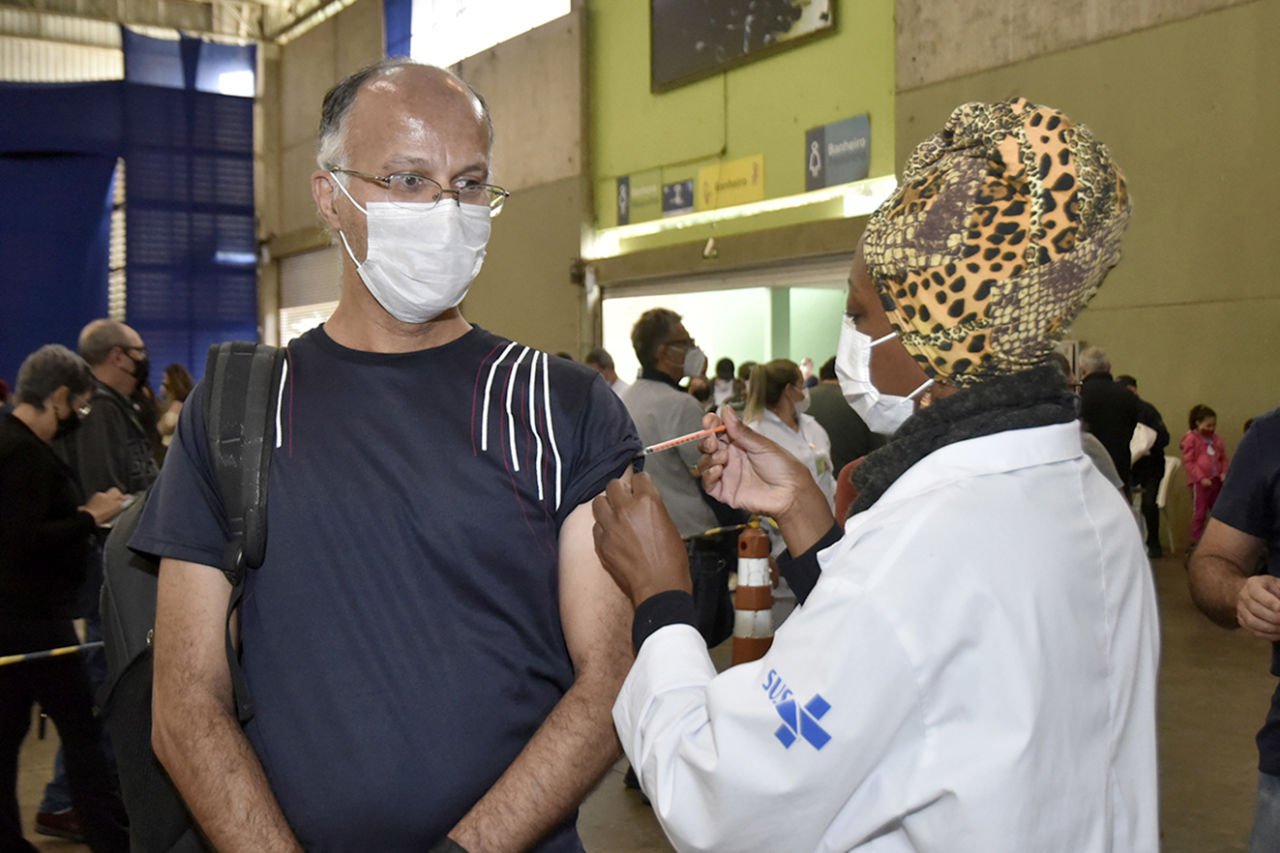 homem de máscara recebe vacina aplicada por enfermeira