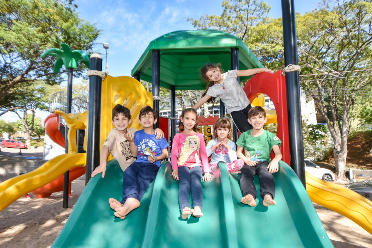 Crianças posam para foto no escorregador do plaground, três meninas e três meninos