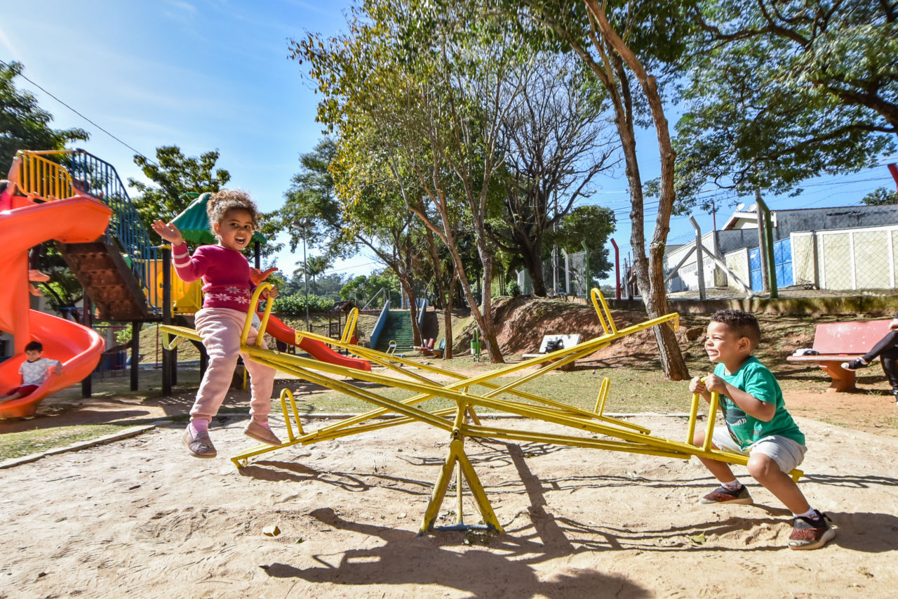 Um menino e uma menina de 4 anos brincam na gangorra do playground
