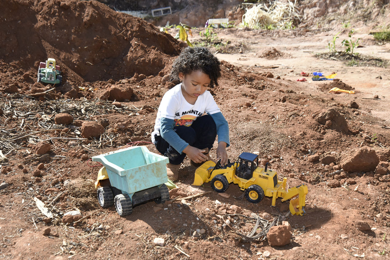 DESCRIÇÃO DA IMAGEM
Garoto está em um terreno com terra, ele brinca com caminhões e maquinários de brinquedos