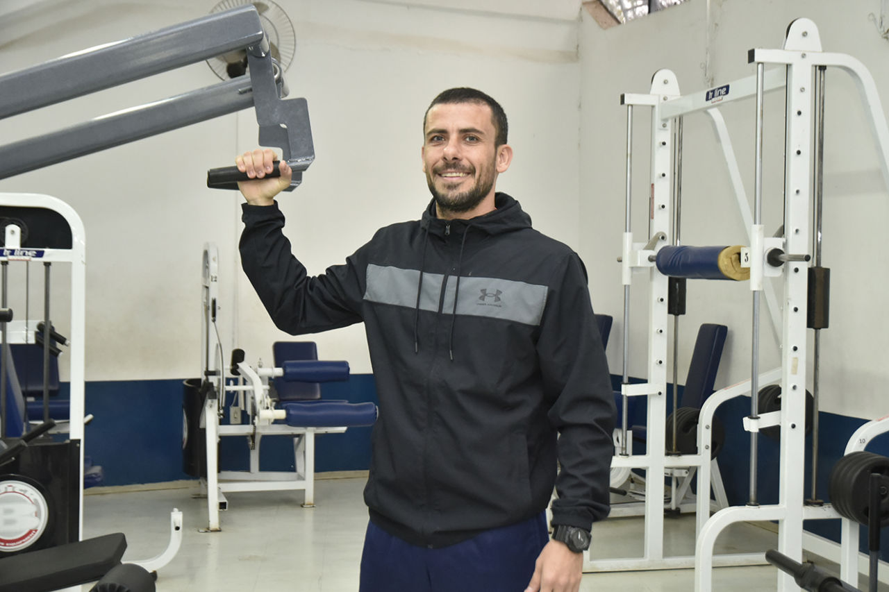 DESCRIÇÃO DA IMAGEM Treinador Bruno se exercitando em um aparelho na academia interna do Bolão