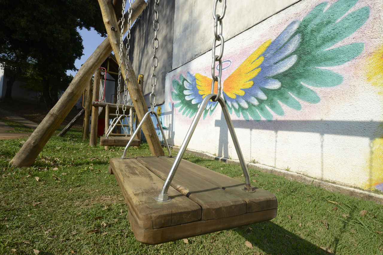 Detalhe de balanço de metal com madeira, com asas coloridas pintadas sobre a parede