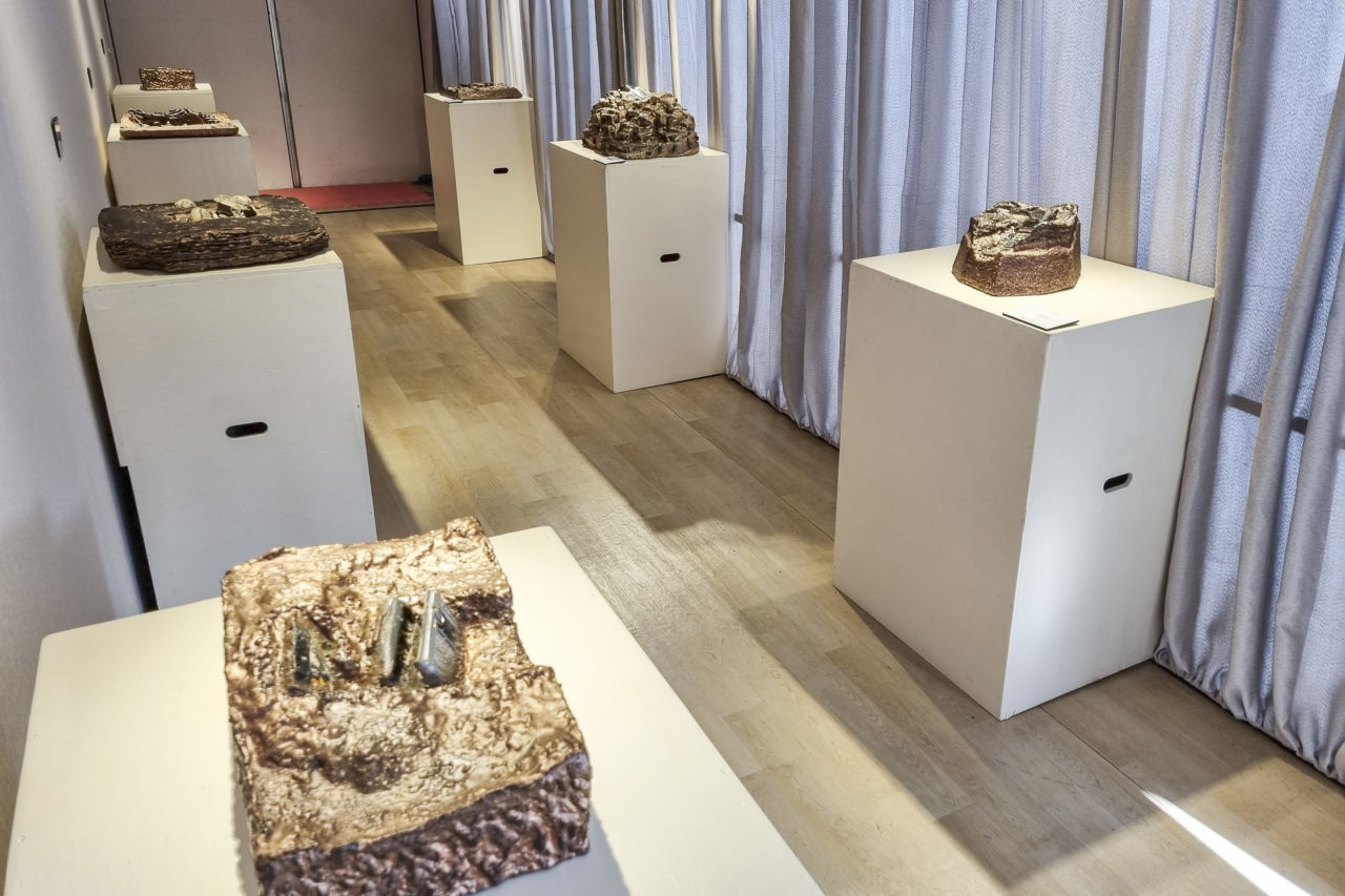 Sala de exposição com peças de material de resina com brilho, posicionadas em estruturas de madeira clara