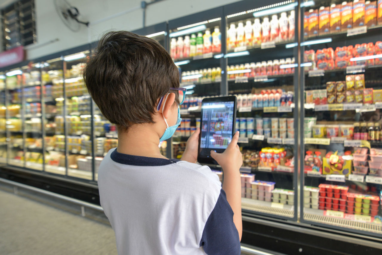 DESCRIÇÃO DA IMAGEM
Estudante está de costas, com tablet na mão. Ele está tirando uma foto de uma geladeira de supermercado.