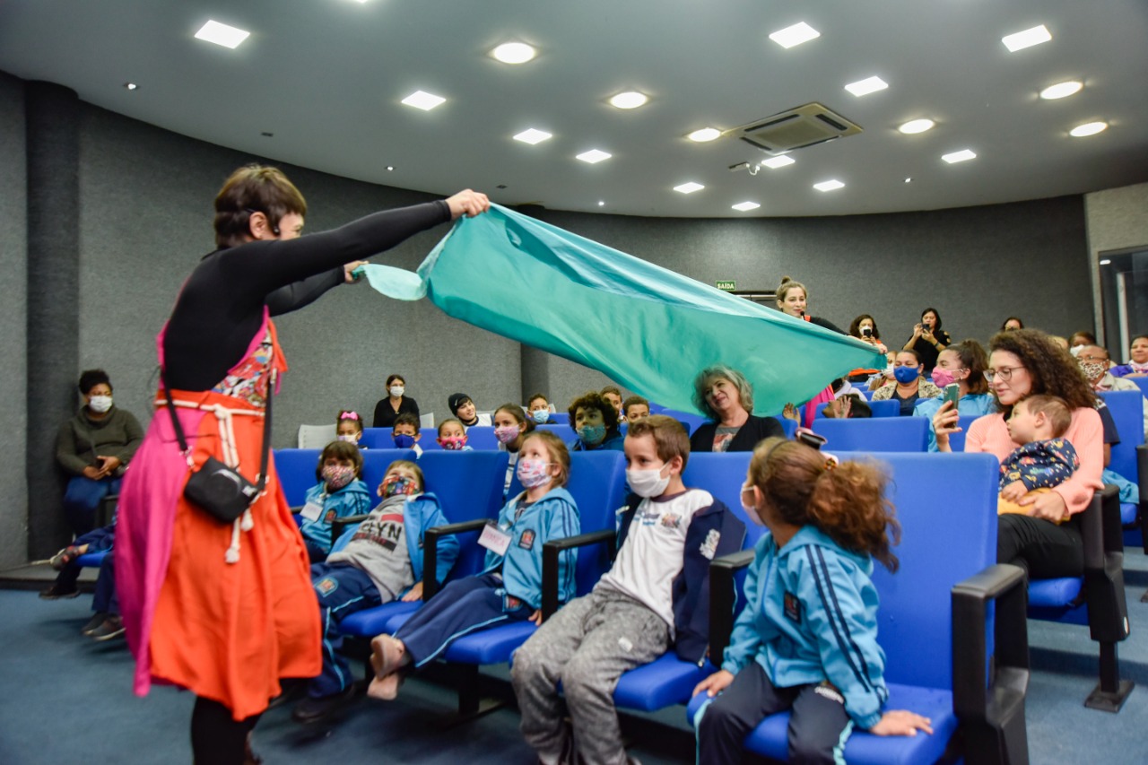 DESCRIÇÃO DE IMAGEM: foto do auditório da Biblioteca Nelson Foot, com crianças sentadas nas poltronas acompanhando a apresentação de artista