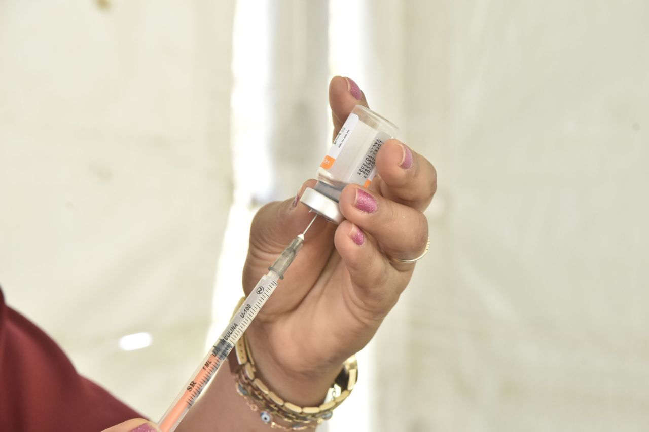 DESCRIÇÃO DE IMAGEM: Mãos manipulam ampola de vacina Coronavac e seringa