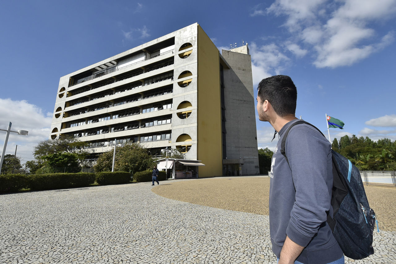 DESCRIÇÃO DE IMAGEM: jovem estudante, de costas, observa o prédio do Paço Municipal