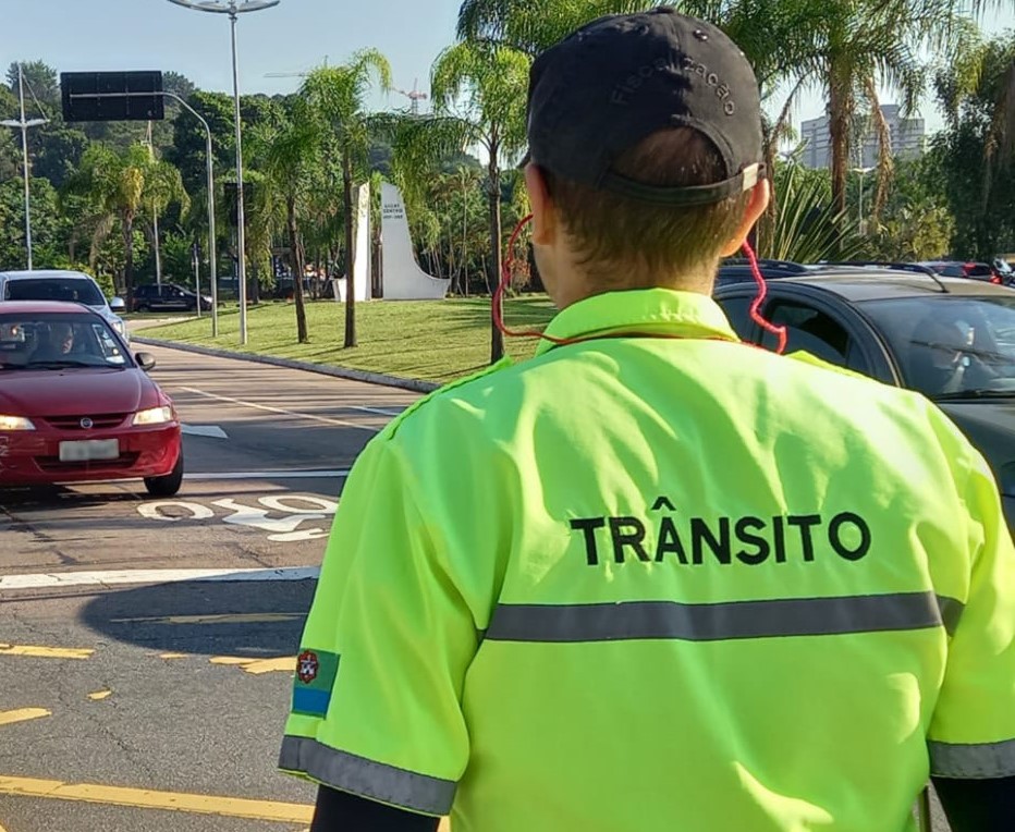 DESCRIÇÃO DE IMAGEM: Agente de trânsito com uniforme verde luminoso, de costas, orienta o trânsito de veículos na avenida Jundiaí