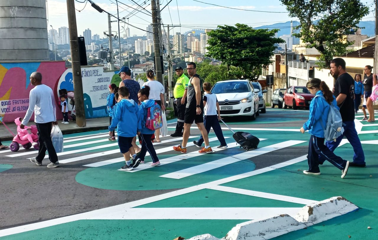 Na foto, o agente de trânsito está atento sobre a faixa de pedestres para que pais e alunos possam atravessar com segurança.
