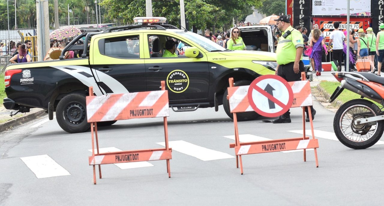 Na foto, agentes de trânsito estão em rua interditada para desfile de bloco de Carnaval, monitorando o movimento para garantir segurança para foliões.