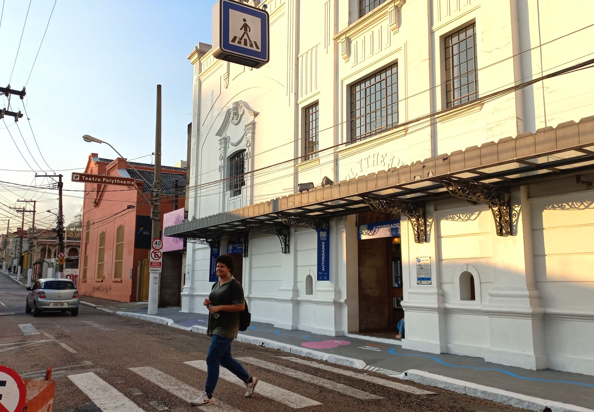 Na imagem, pedestre atravessa na faixa que conta com luminária em frente ao Teatro Polytheama.