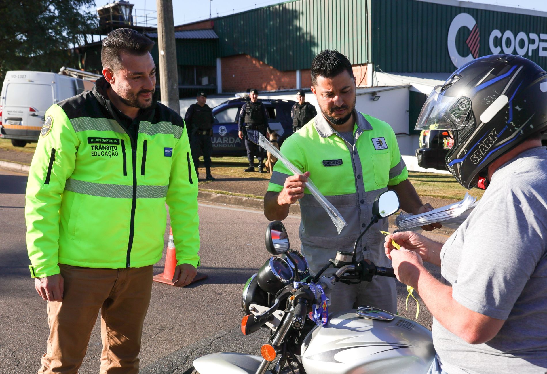 Na imagem, o operador de máquinas Wesley, está sobre a moto, e recebe um kit com antena corta-pipa, adesivo e fita do Maio Amarelo, durante uma ação educativa para promover a segurança no trânsito.