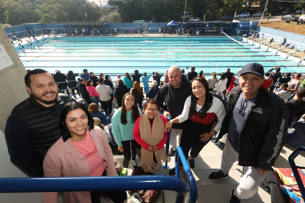 Pessoas posando para a foto, sorrindo. Ao fundo, piscina do complexo aquático. 
