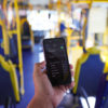 Na imagem, tem uma mão segurando um celular, com a tela inicial com o nome da rede de wi-fi nos ônibus: conect@adobus. Os ônibus municipais de Jundiaí contam com sinal de internet de graça para os usuários.