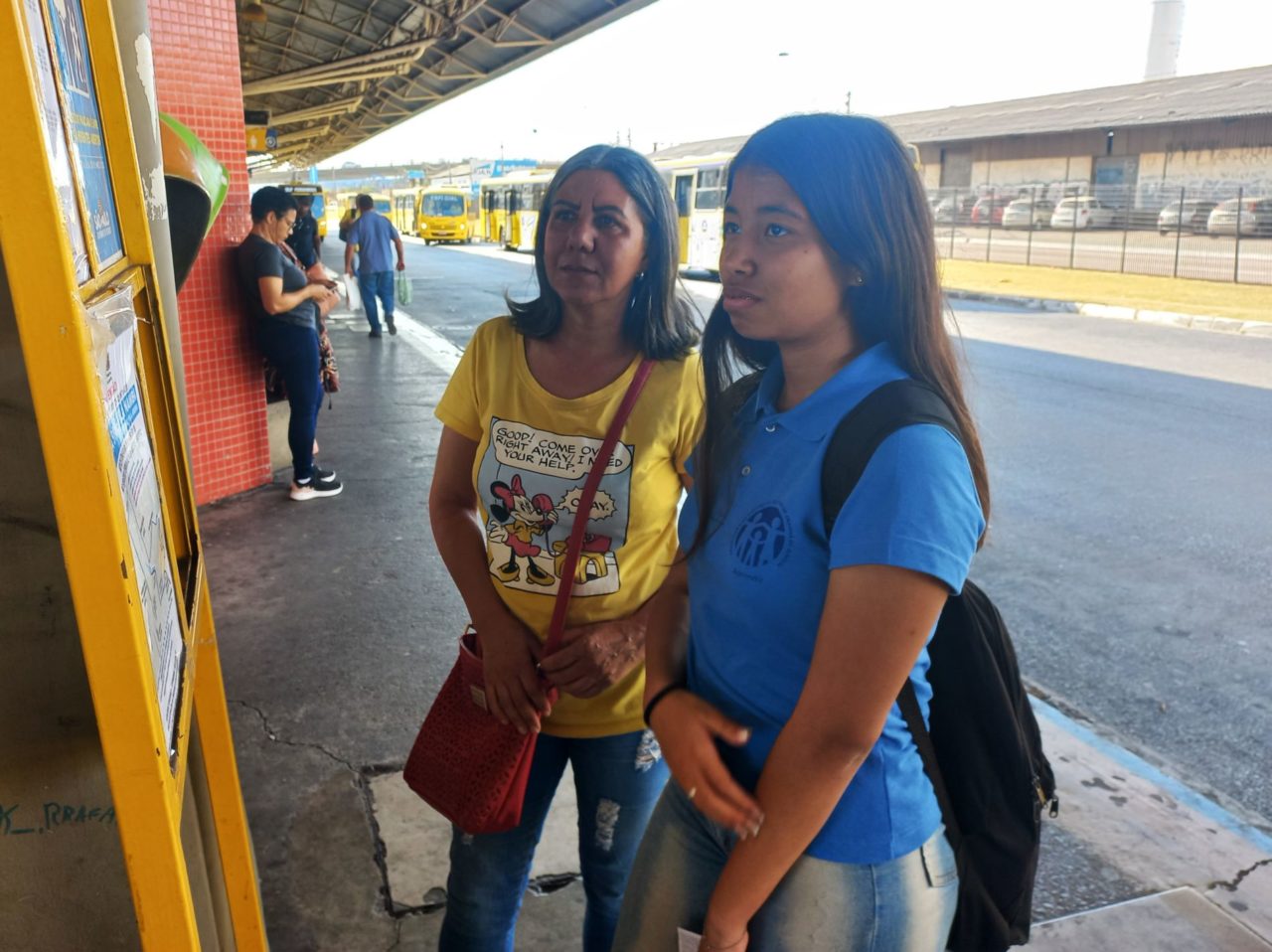 Na imagem estão duas mulheres na plataforma, e elas verificam no painel os horários de ônibus. As duas elogiaram os novos itinerários com expectativa de chegar mais cedo em casa.