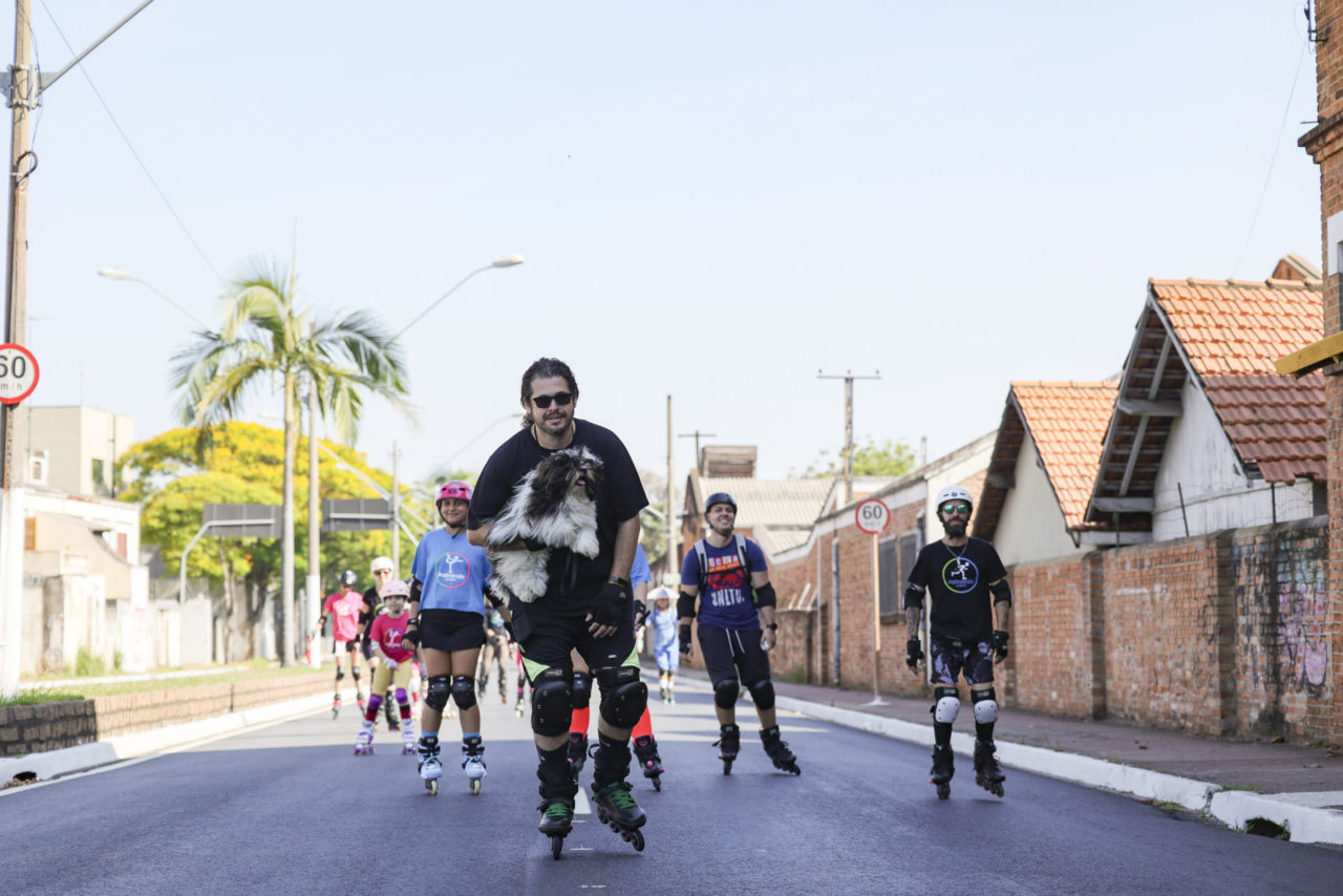 A imagem mostra um jovem de patins com um cachorro na mão direita, e outras pessoas de patins atrás. Evento Mobilidade Saudável e Lazer levou diversão e convivência a ruas da Vila Arens e Centro.