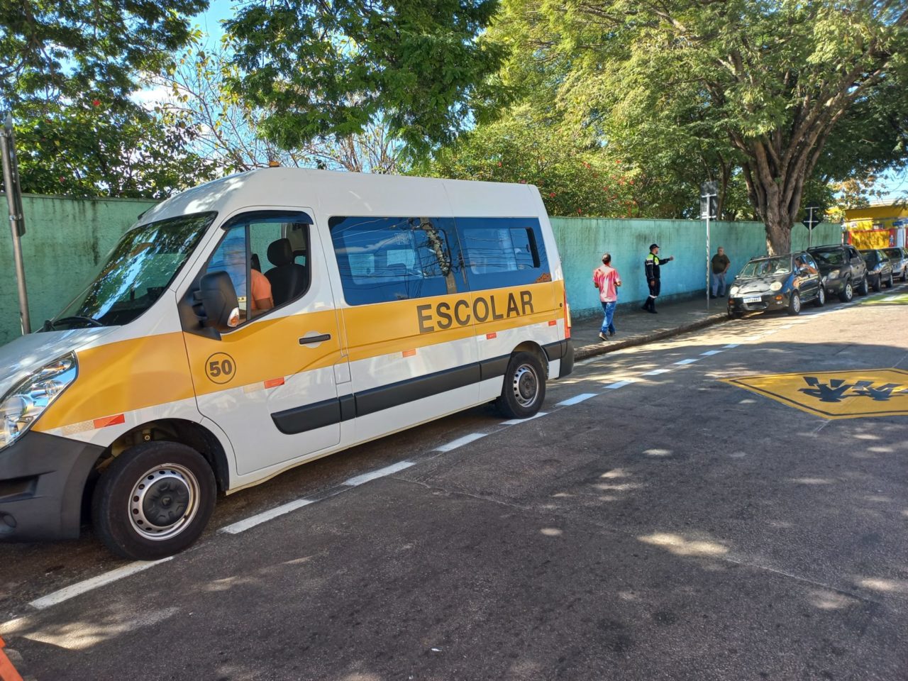 A imagem mostra uma van escolar estacionada em frente a uma escola na Vila Rio Branco, tem também crianças andando na calçada. É para informar que tem inscrições abertas até 30 de setembro para alvará de transporte escolar.