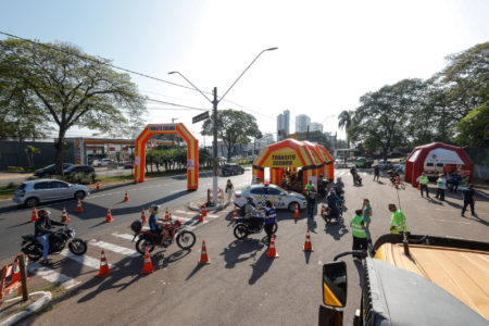 A imagem mostra o bolsão do Parque da Uva com duas tendas com a escrita - trânsito seguro - onde motociclistas pararam para receberem orientações e a colocação de antenas corta-pipas em suas motos. A ação do departamento de Trânsito da Unidade de Gestão de Mobilidade e Transporte, em parceria com a CCR AutoBan, Detran SP, Polícia Militar e Polícia Militar Rodoviária, nesta quinta-feira (21).