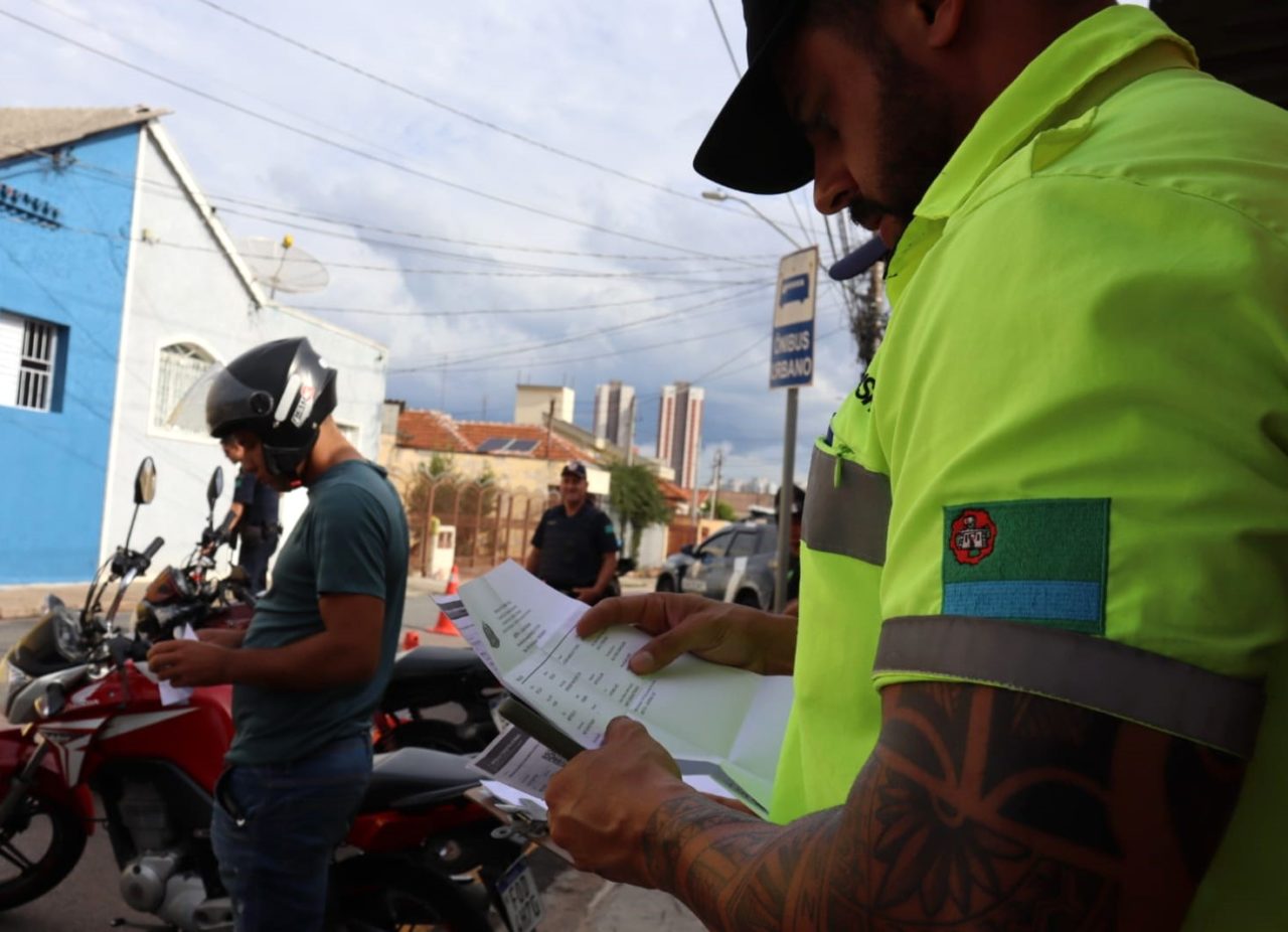 A imagem mostra um agente verificando a documentação de uma moto em uma operação de fiscalização contra motos barulhentas em Jundiaí.