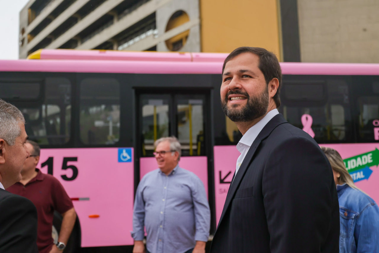 A imagem mostra o prefeito Luiz Fernando Machado em frente ao Paço, e o ônibus rosa e azul atrás