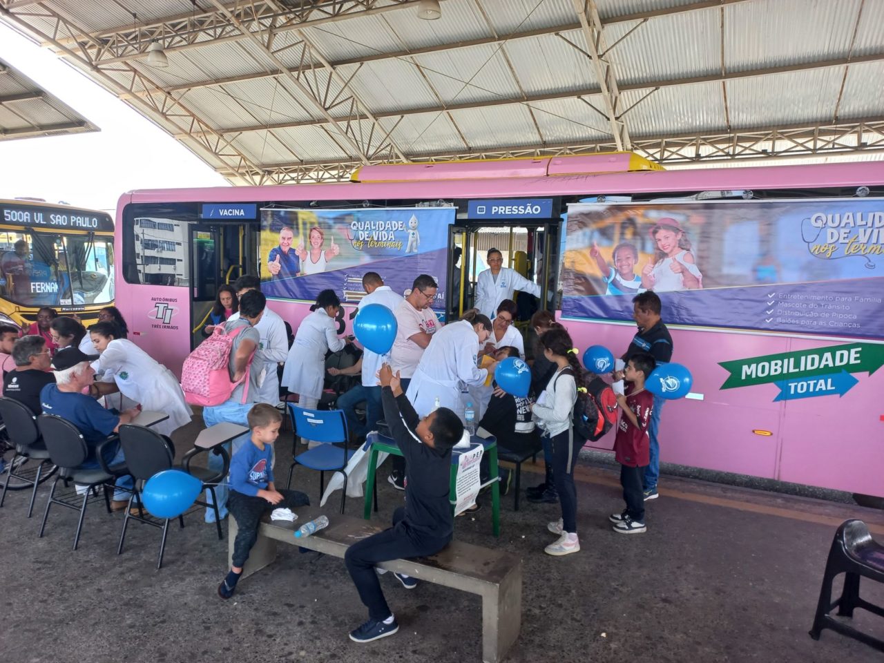 A imagem mostra várias pessoas na plataforma do Terminal Vila Arens, um ônibus rosa e azul, no Qualidade de Vida nos Terminais.