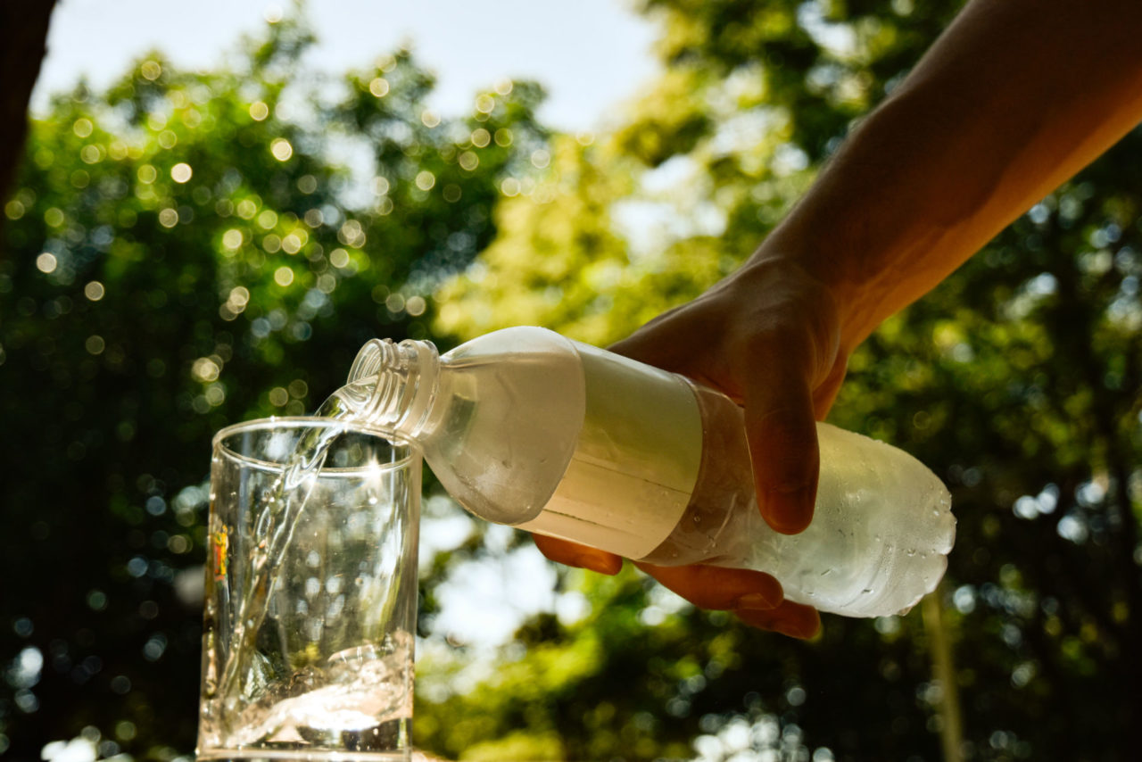 Pessoa derramando água de uma garrafa para um copo.
