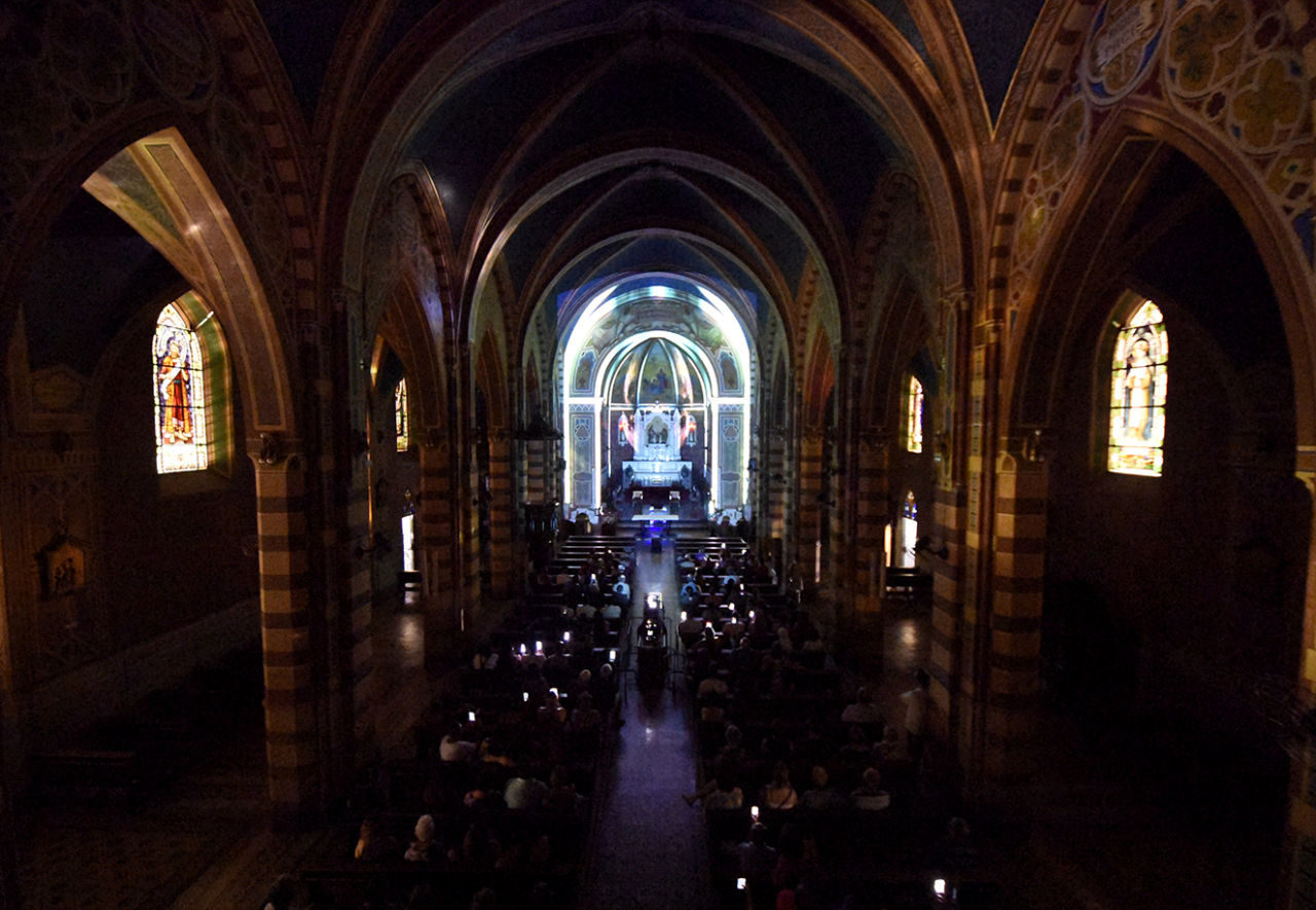 Interior de igreja no escuro, com projeções luminosas coloridas sobre as paredes